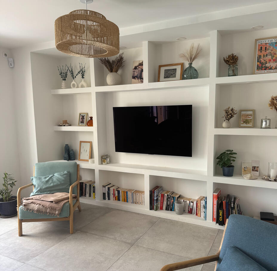 Salon avec bibliothèque murale blanche sur mesure intégrant la télévision, fauteuil bleu et plantes, agencement Atelier Luzons