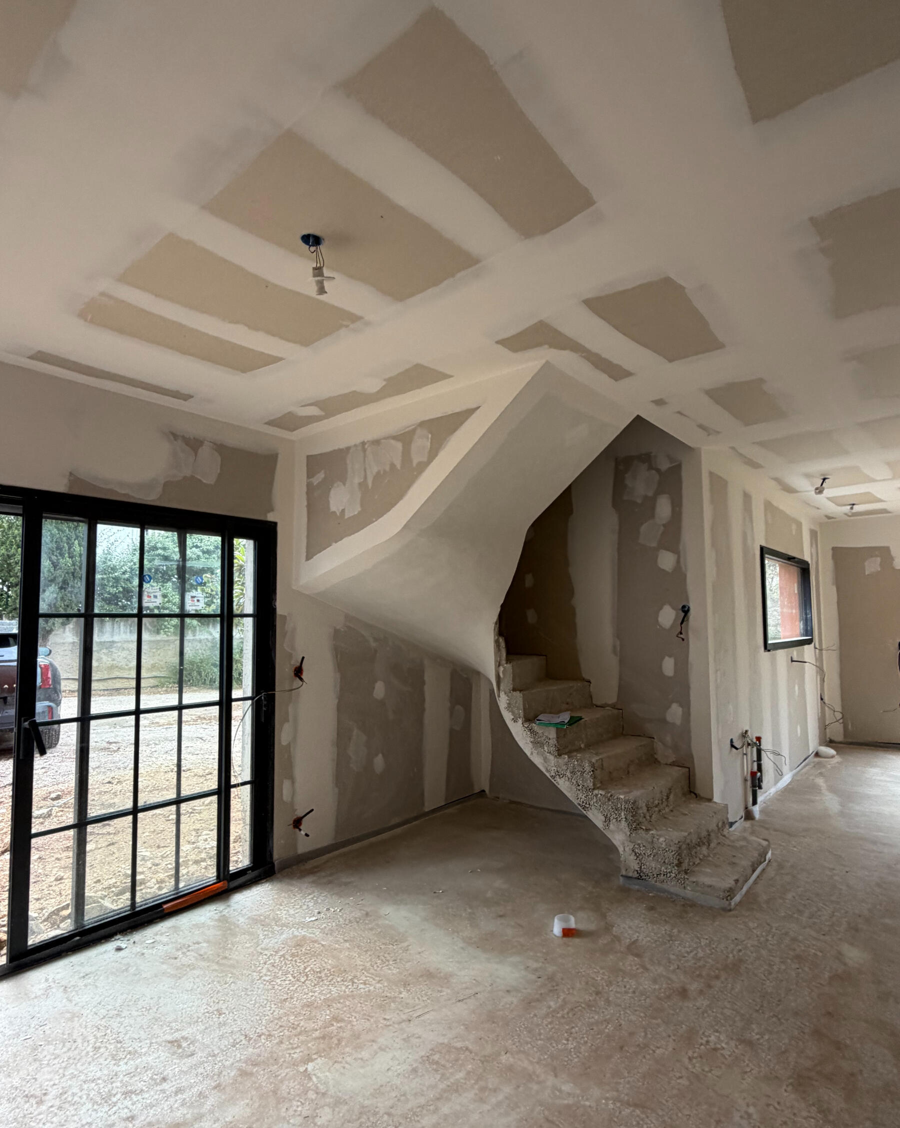 Salon en cours de rénovation avec escalier hélicoïdal et grande baie vitrée, chantier suivi par Atelier Luzons à Marseille